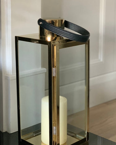 Gold and glass lantern with black leather strap/handle in lifestyle photo