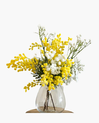 Faux flower arrangement of mimosa and babys breath in glass vase on white background