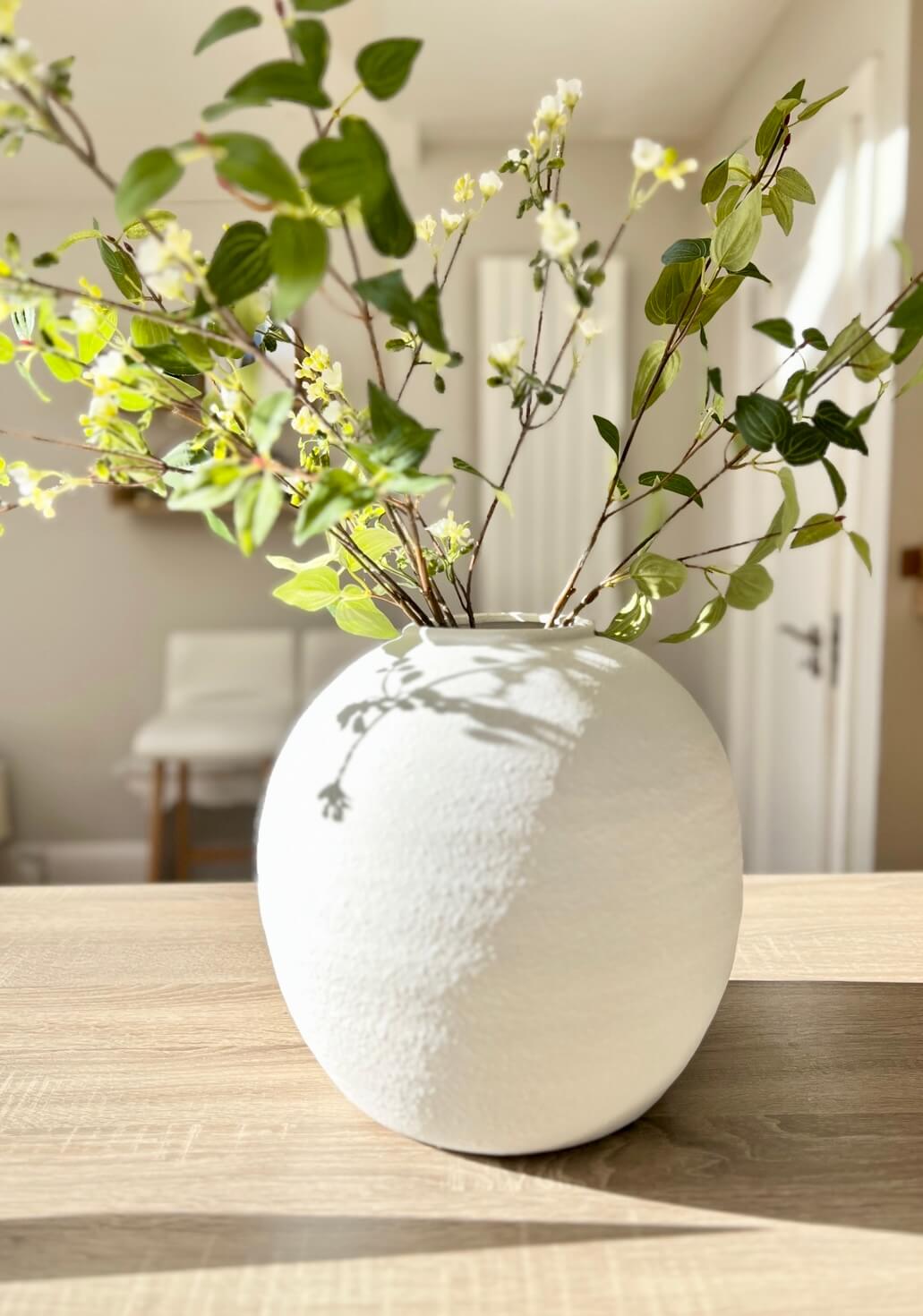 Stems of green foliage in white vase on lifestyle background